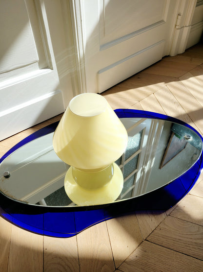 top view of an ochre yellow swirl Murano mushroom table lamp on a mirror with cobalt blue edging. 