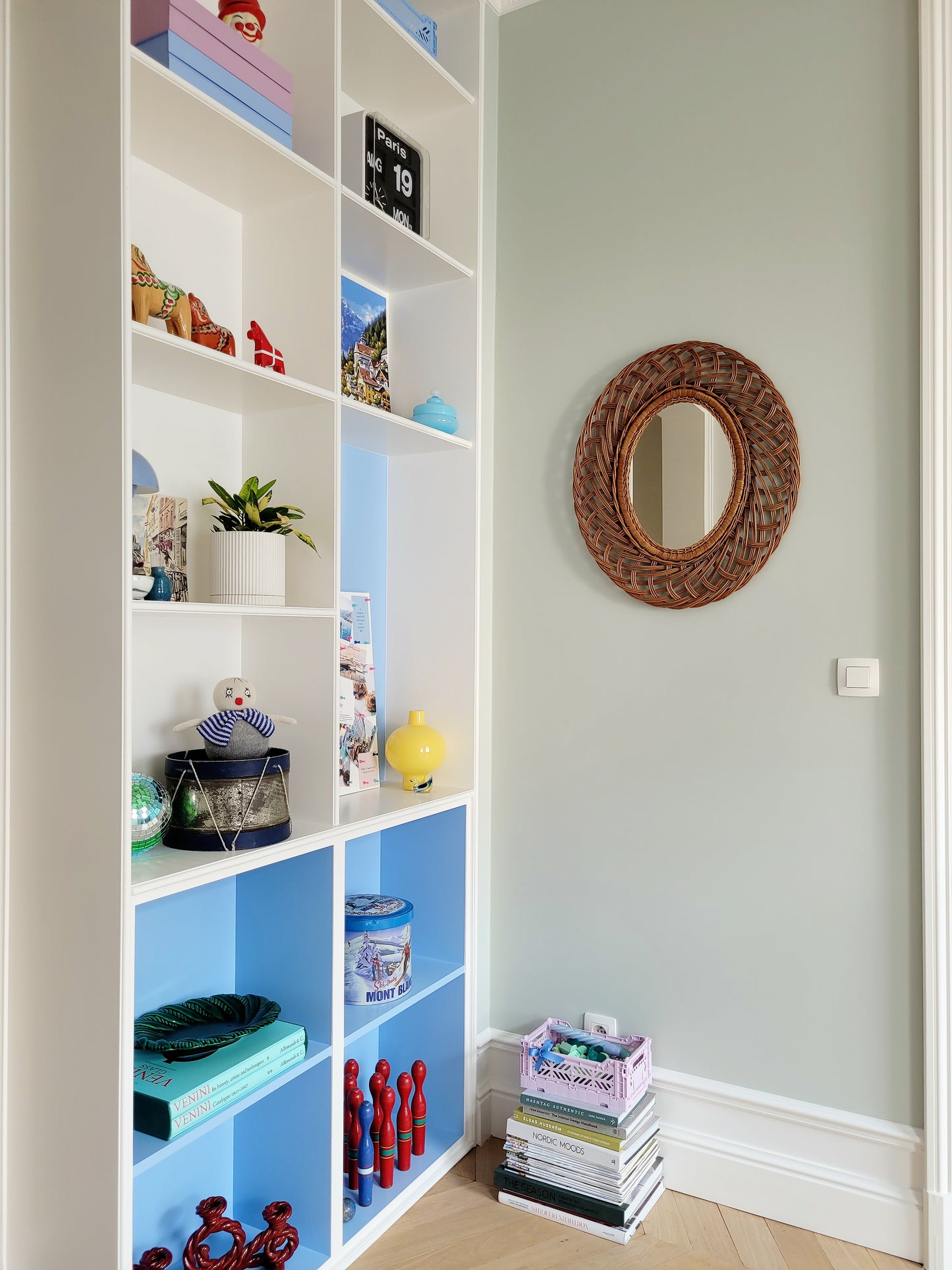 full view of a mid century large oval wall mirror next to filled colourful cabinets