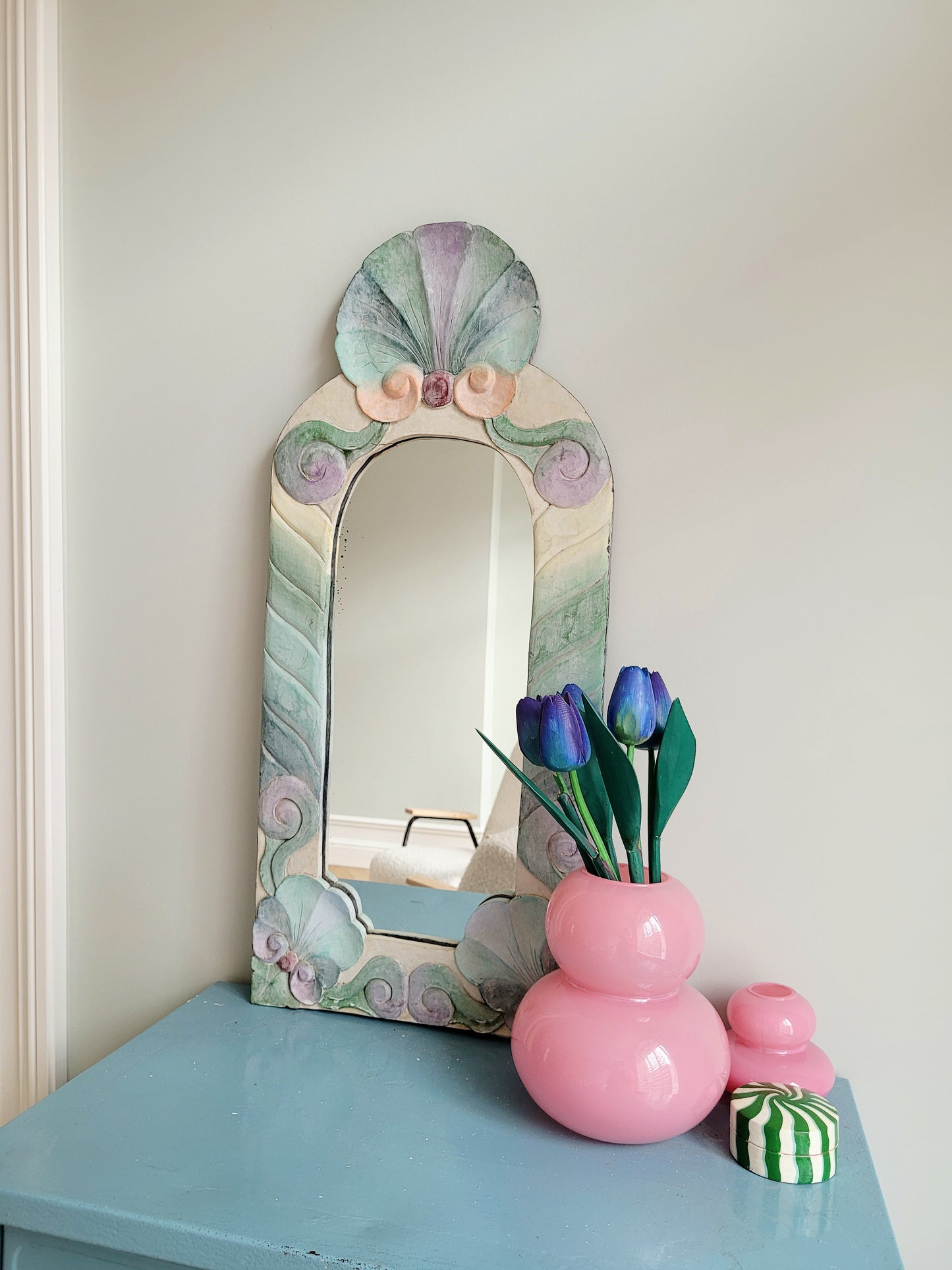 full view of a pastel coloured wooden wall mirror with flower design next to a pink vase with wooden tulips