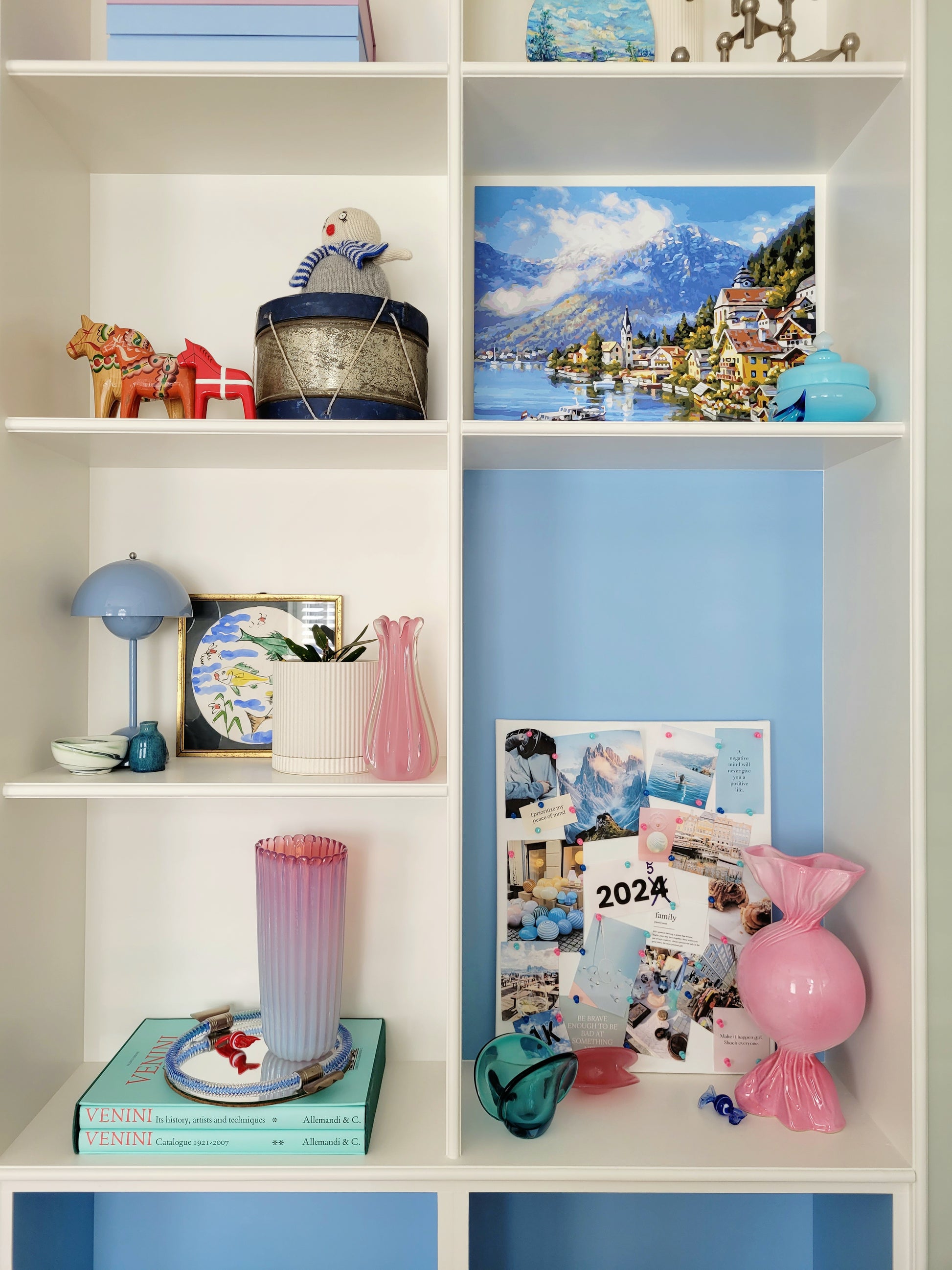 full view of a built-in cabinet filled with vintage interior objects, Murano items and souvenirs, with a pink ceramic candy bonbon vase and a vision board next to it