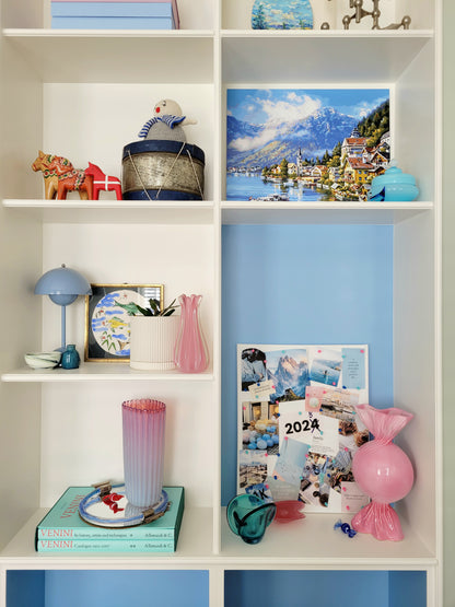 full view of a built-in cabinet filled with vintage interior objects, Murano items and souvenirs, with a pink ceramic candy bonbon vase and a vision board next to it