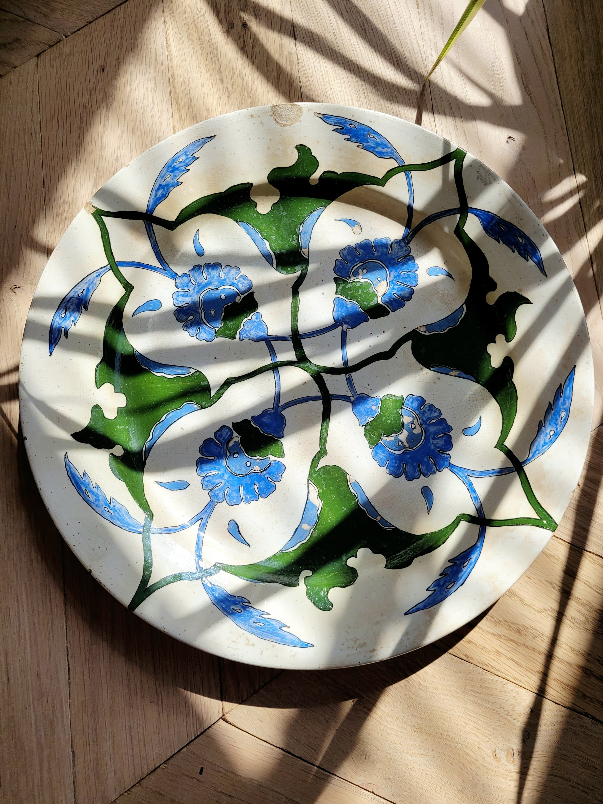detailof a vintage Italian (wall) plate with blue and green floral motif on a parquet floor with rays of sunshine