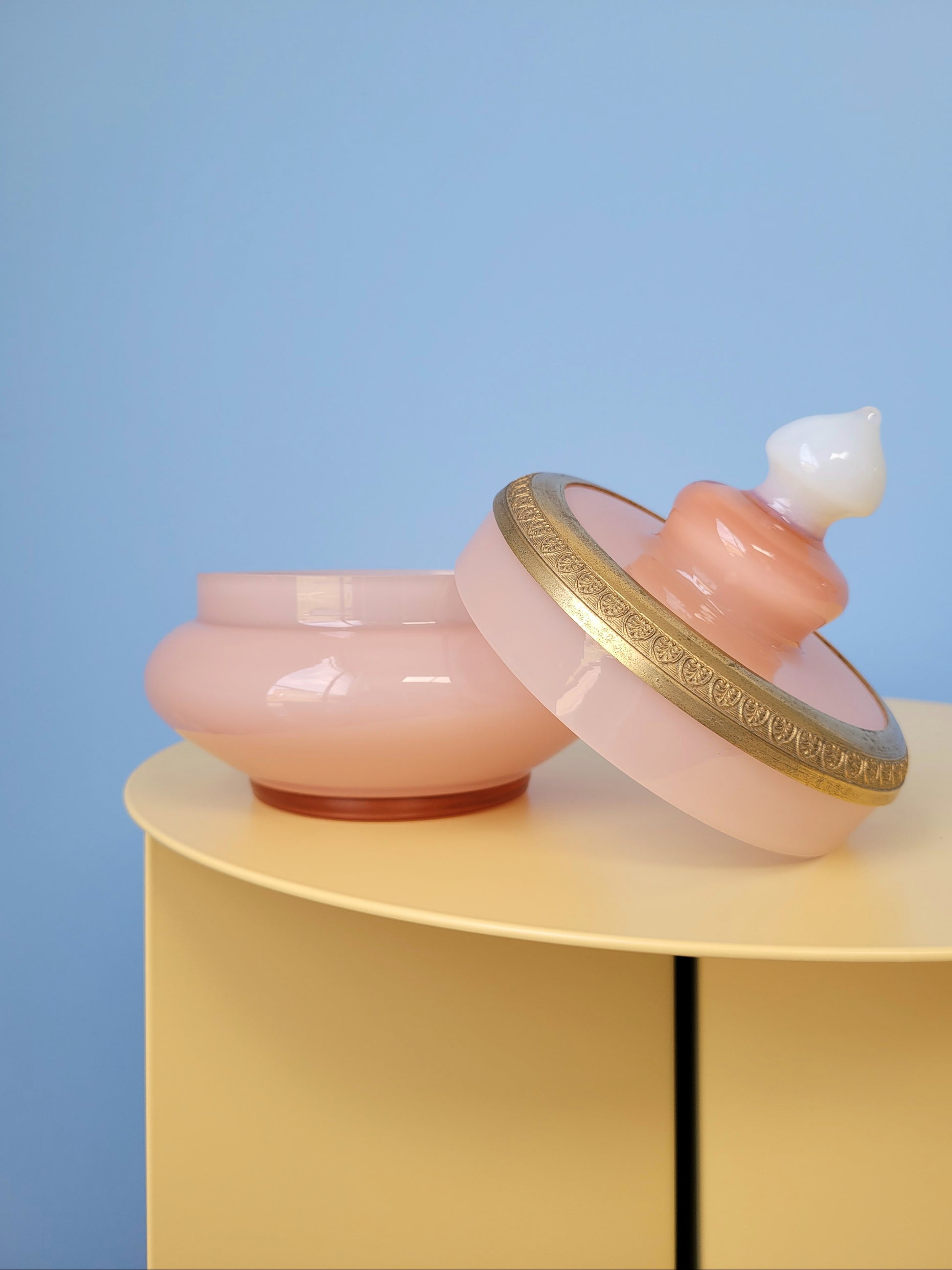 front view of a vintage opal pink glass bonbonniere with open lid on a yellow side table