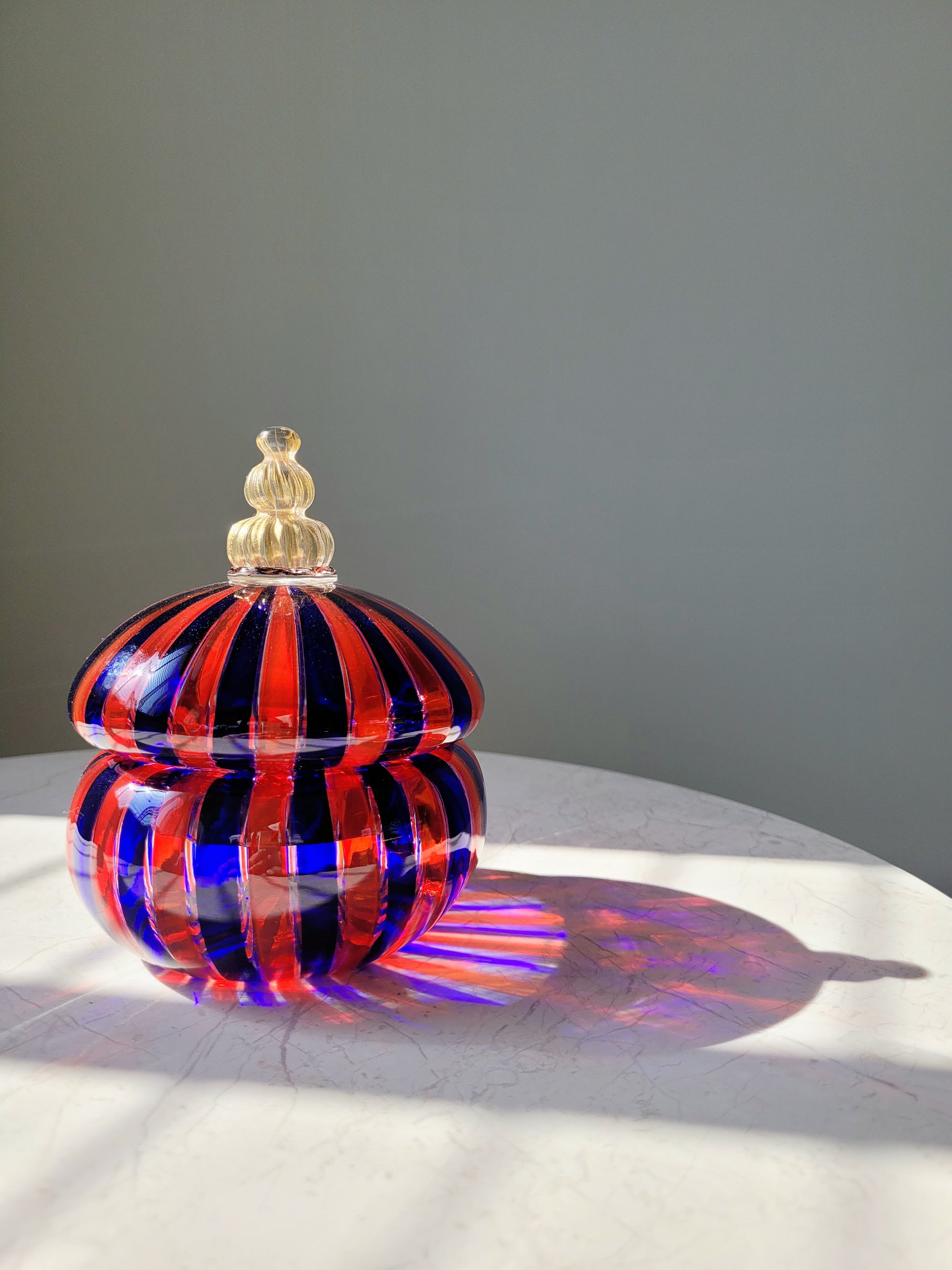 front view of a handcrafted vintage striped Murano bonbonniere in red blue and gold 