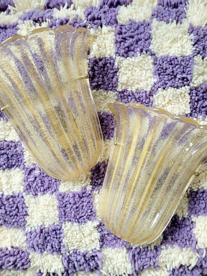 top view of a pair of Barovier & Toso Murano glass wall lamps with a leaf design. The lamps are placed on a pouf with a purple and white checkerboard pattern.