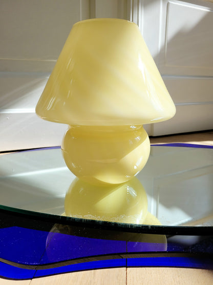 front view of an ochre yellow swirl Murano mushroom table lamp on a mirror with cobalt blue edging. 