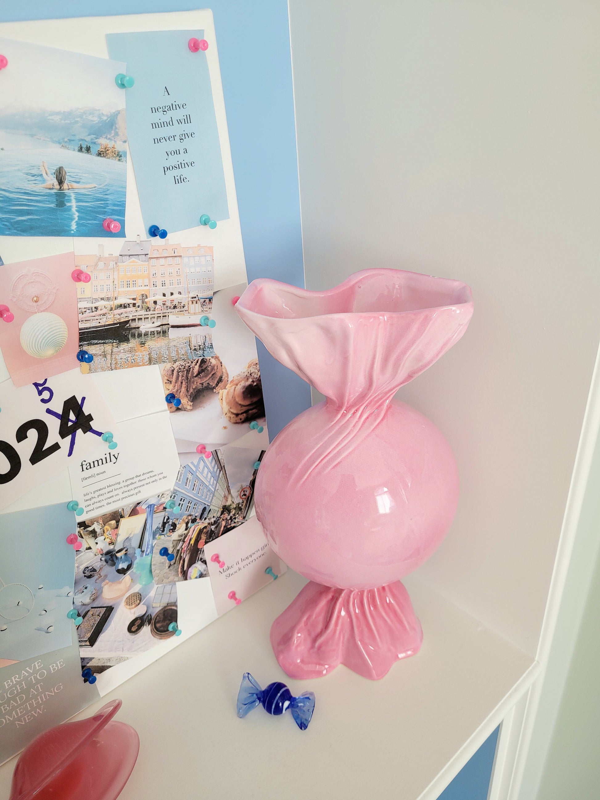 side view of a pink ceramic candy bonbon vase with a vision board next to it and a small Murano candy in the front