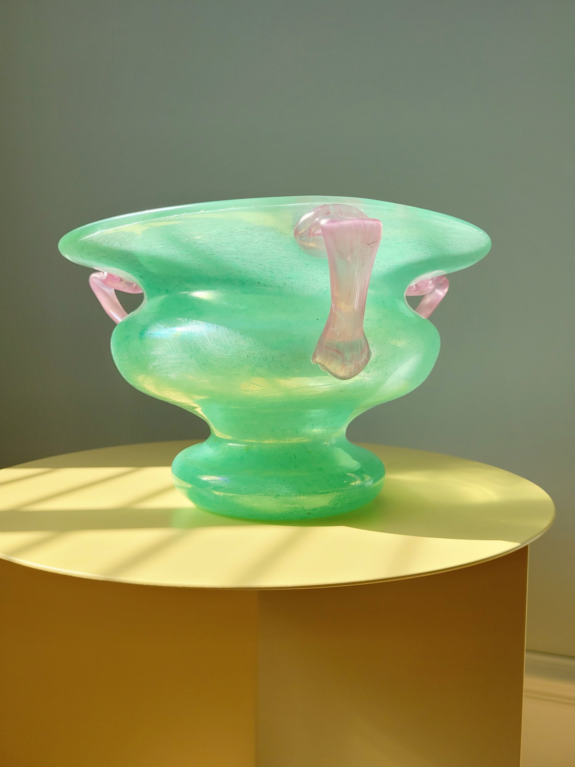 side view of a scavo Murano glass amphora vase in green and pink on a yellow side table
