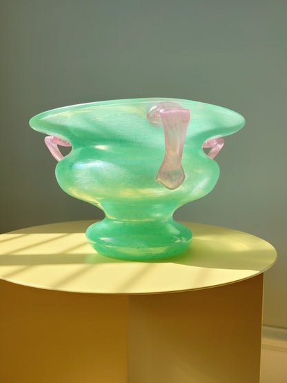 side view of a scavo Murano glass amphora vase in green and pink on a yellow side table
