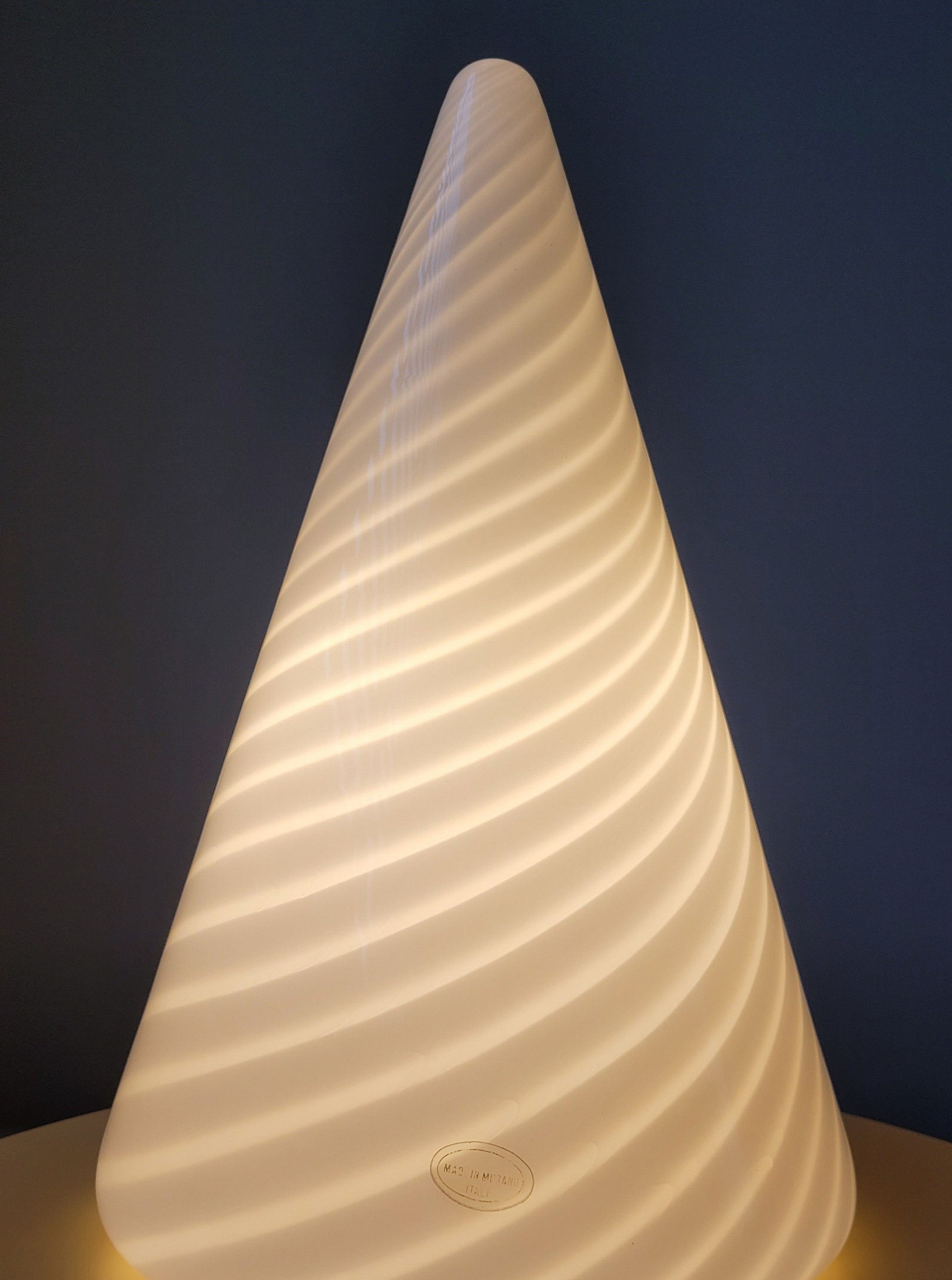 detail of an illuminated vintage Murano cone lamp with white and translucent swirl on a yellow side table
