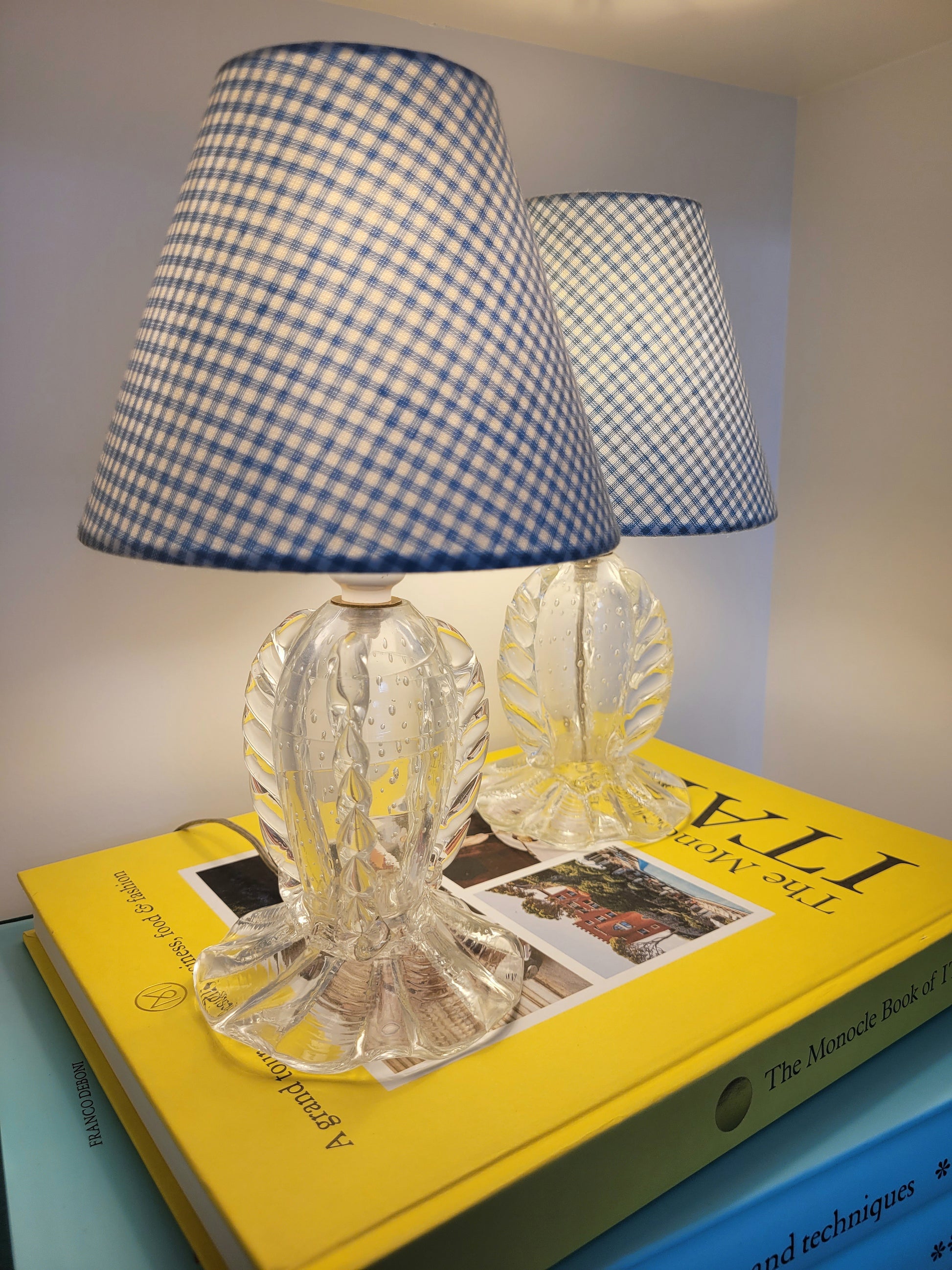 side view of a rare pair of vintage clear Murano table lamps with shades stacked on books illuminated