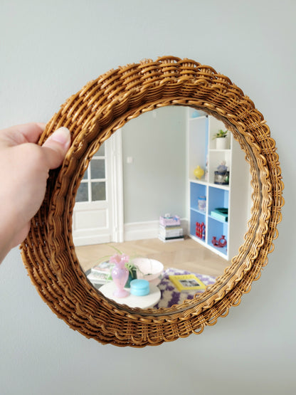 side view of a vintage woven round wall mirror stacked on top of a pile of books handheld