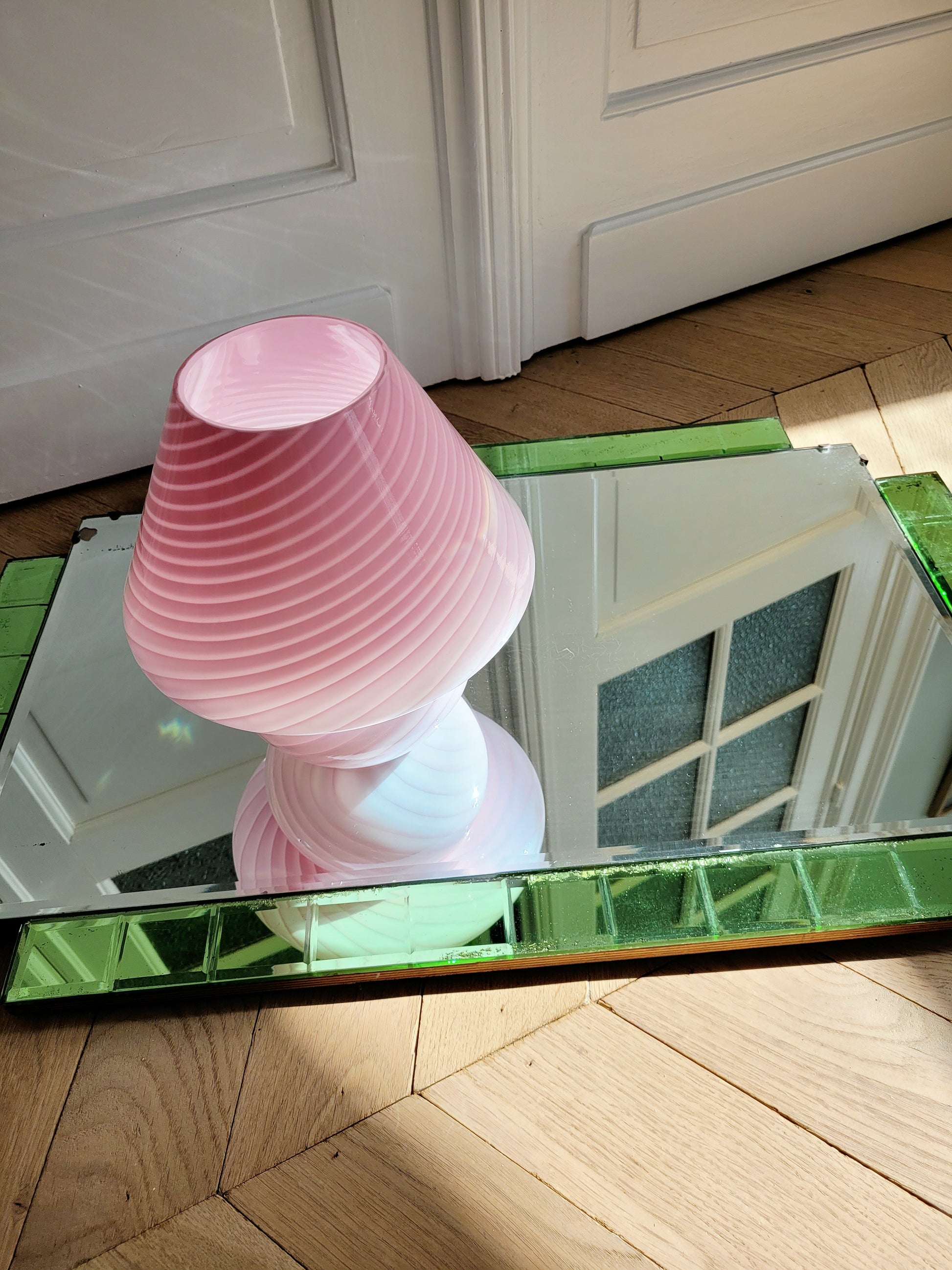 top view of a pink and white swirl Murano mushroom table lamp on a mirror with green edging. 