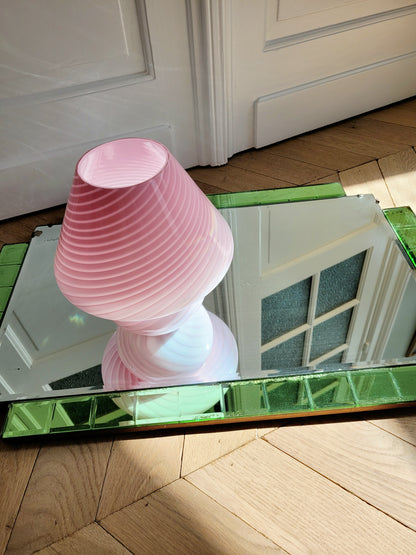 top view of a pink and white swirl Murano mushroom table lamp on a mirror with green edging. 