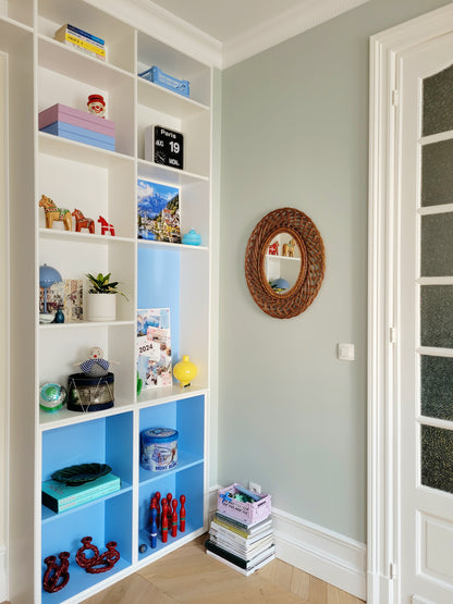full view of a mid century large oval wall mirror next to filled colourful cabinets