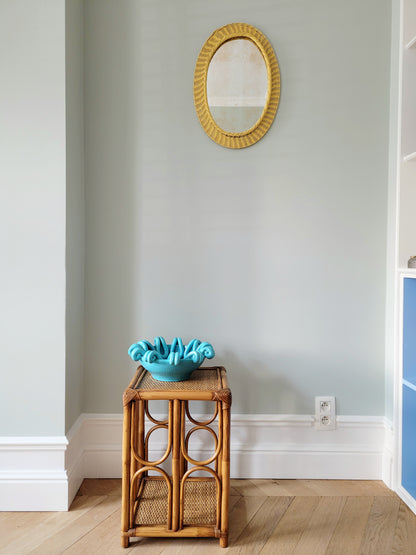 full view of a striking turquoise ceramic serving bowl on a bamboo side table and yellow mirror on wall