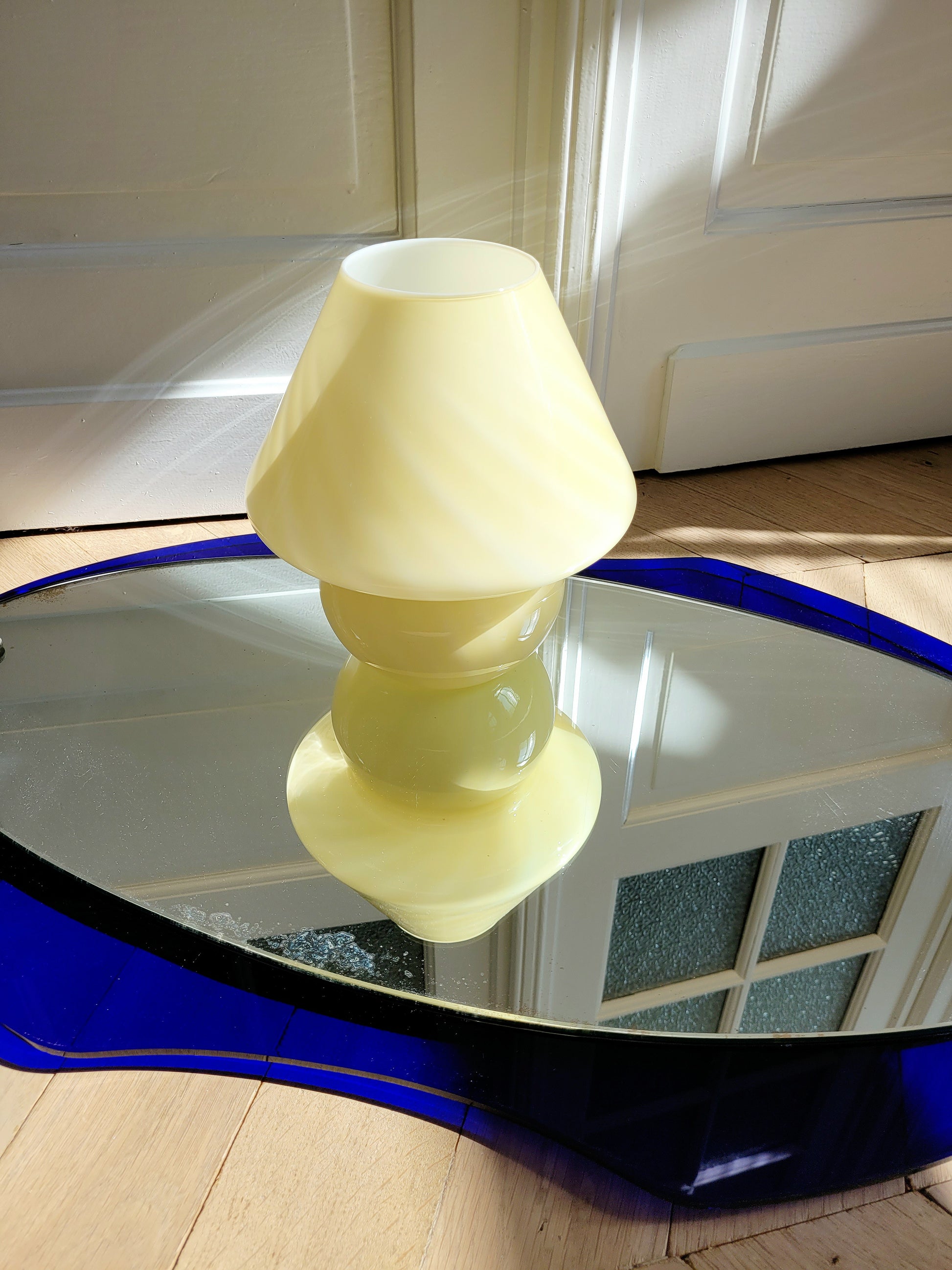 top view of an ochre yellow swirl Murano mushroom table lamp on a mirror with cobalt blue edging. 