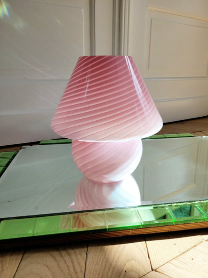 front view of a pink and white swirl Murano mushroom table lamp on a mirror with green edging. 