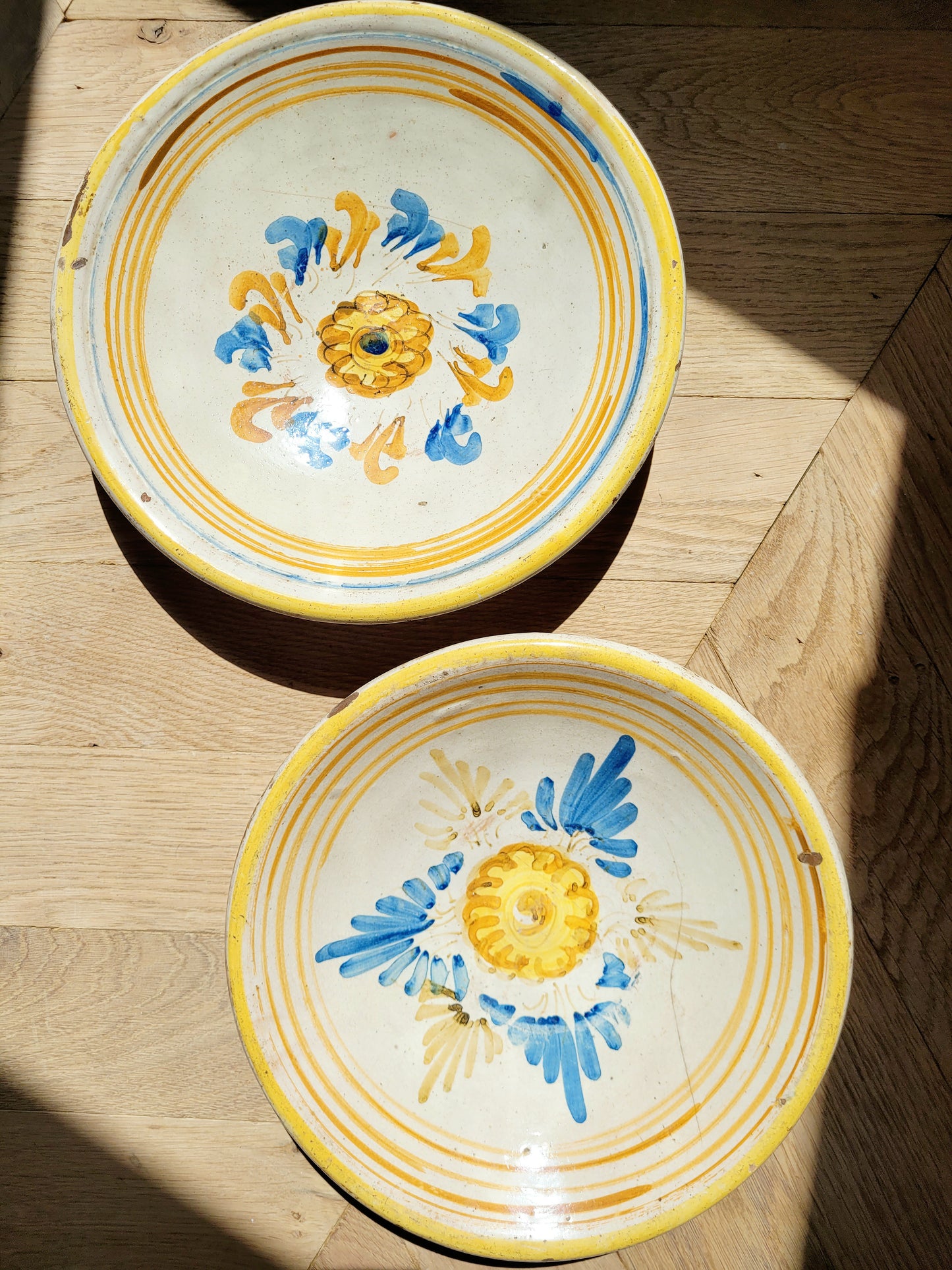 full view of a pair of antique ceramic (wall) plates, adorned in vibrant blue and yellow hues with a stunning flower pattern on a parquet floor