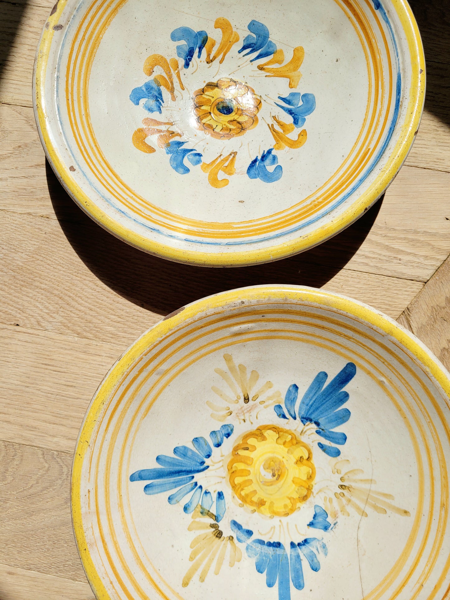 detail of a pair of antique ceramic (wall) plates, adorned in vibrant blue and yellow hues with a stunning flower pattern on a parquet floor