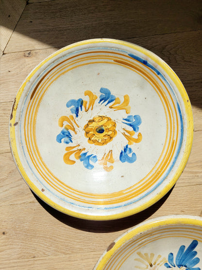 an antique ceramic (wall) plate, adorned in vibrant blue and yellow hues with a stunning flower pattern on a parquet floor