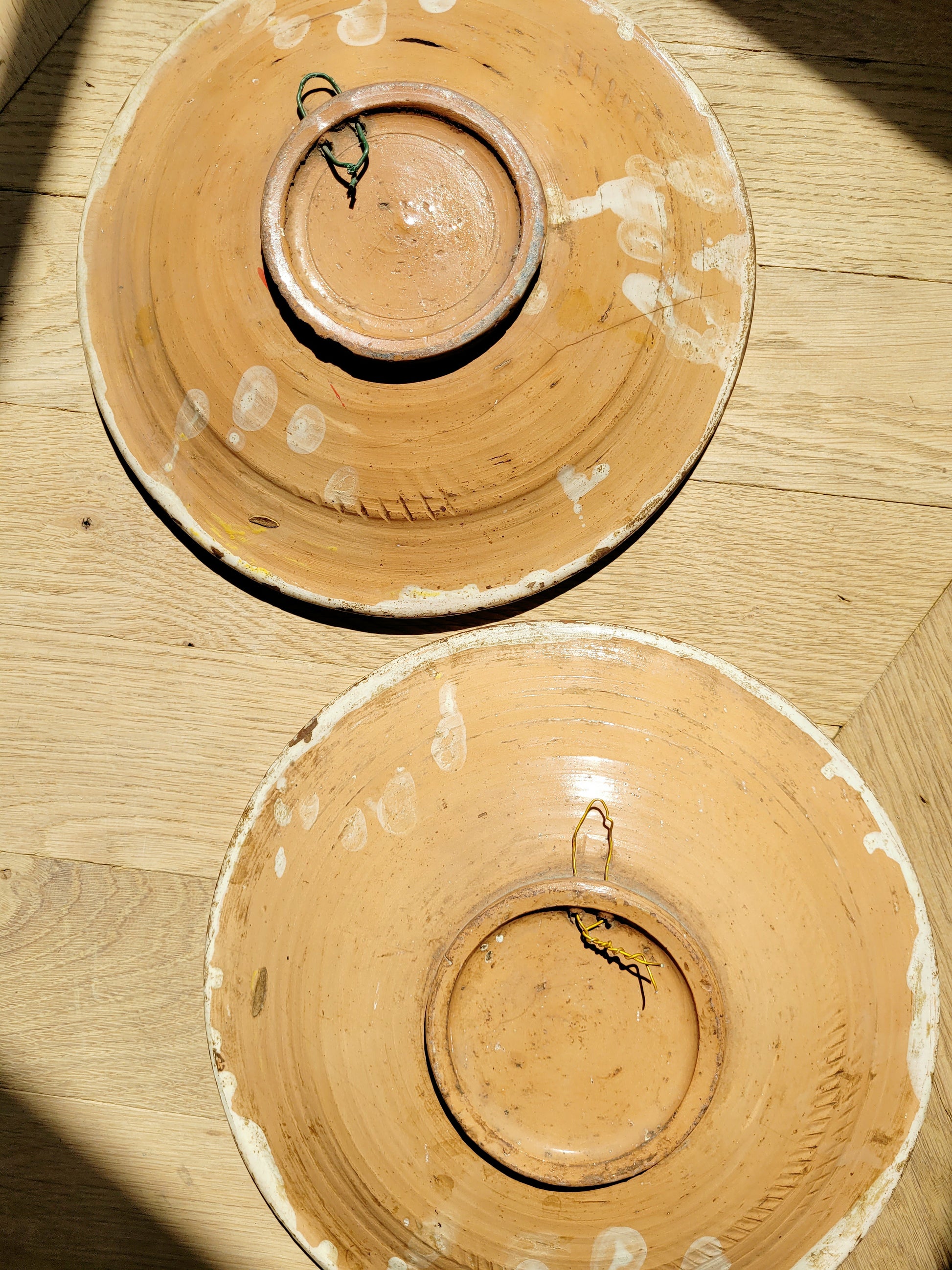 back view of a pair of antique ceramic (wall) plates, adorned in vibrant blue and yellow hues with a stunning flower pattern on a parquet floor