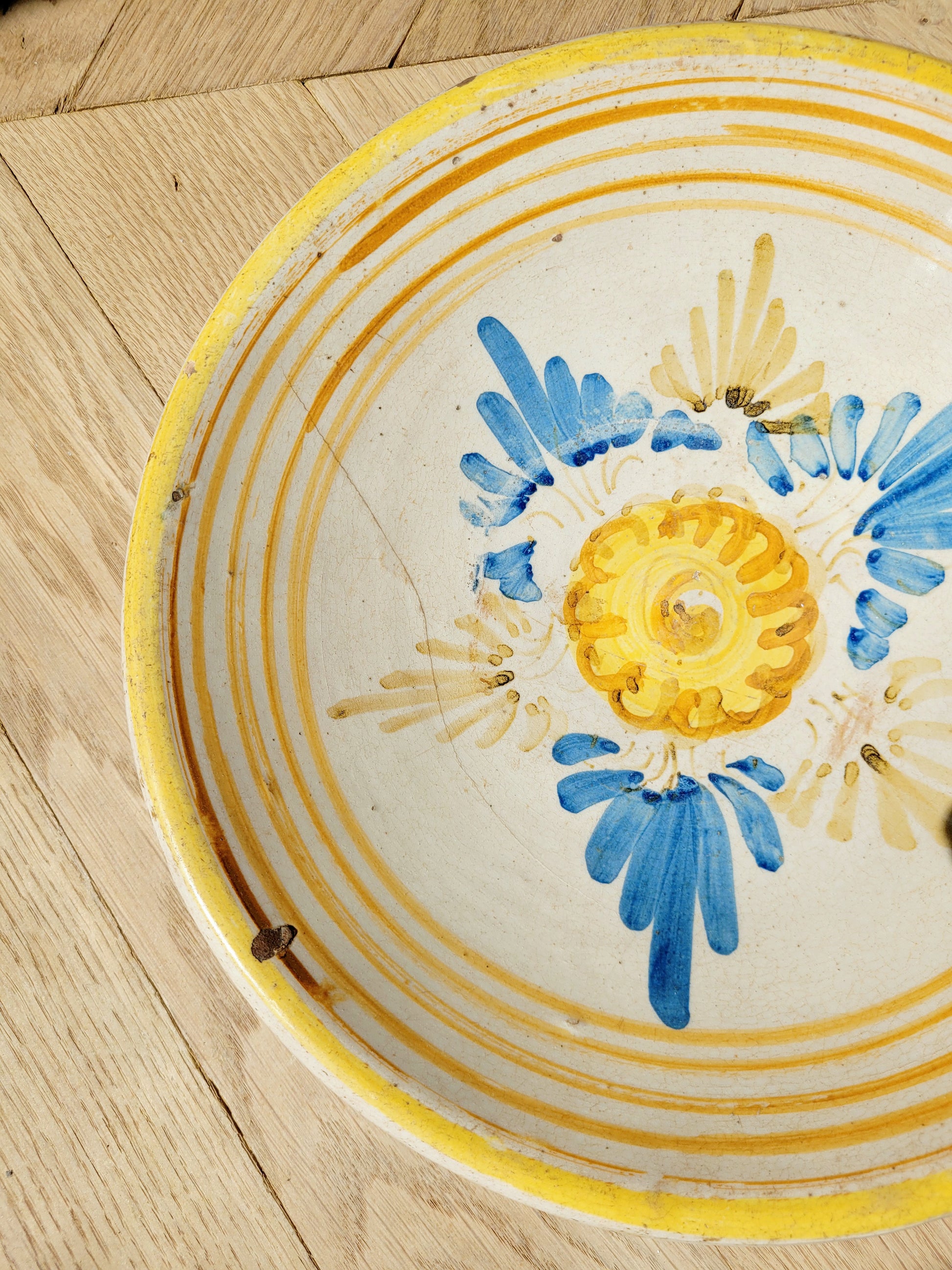 detail of an antique ceramic (wall) plate, adorned in vibrant blue and yellow hues with a stunning flower pattern on a parquet floor