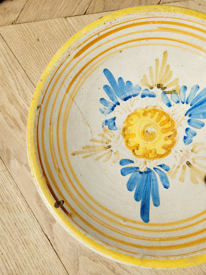 detail of an antique ceramic (wall) plate, adorned in vibrant blue and yellow hues with a stunning flower pattern on a parquet floor