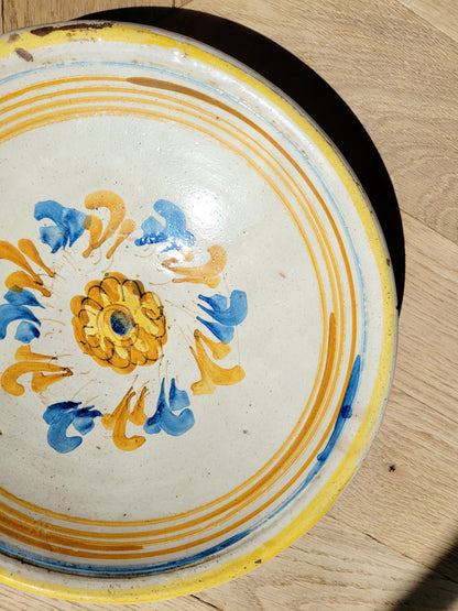 detail of an antique ceramic (wall) plate, adorned in vibrant blue and yellow hues with a stunning flower pattern on a parquet floor