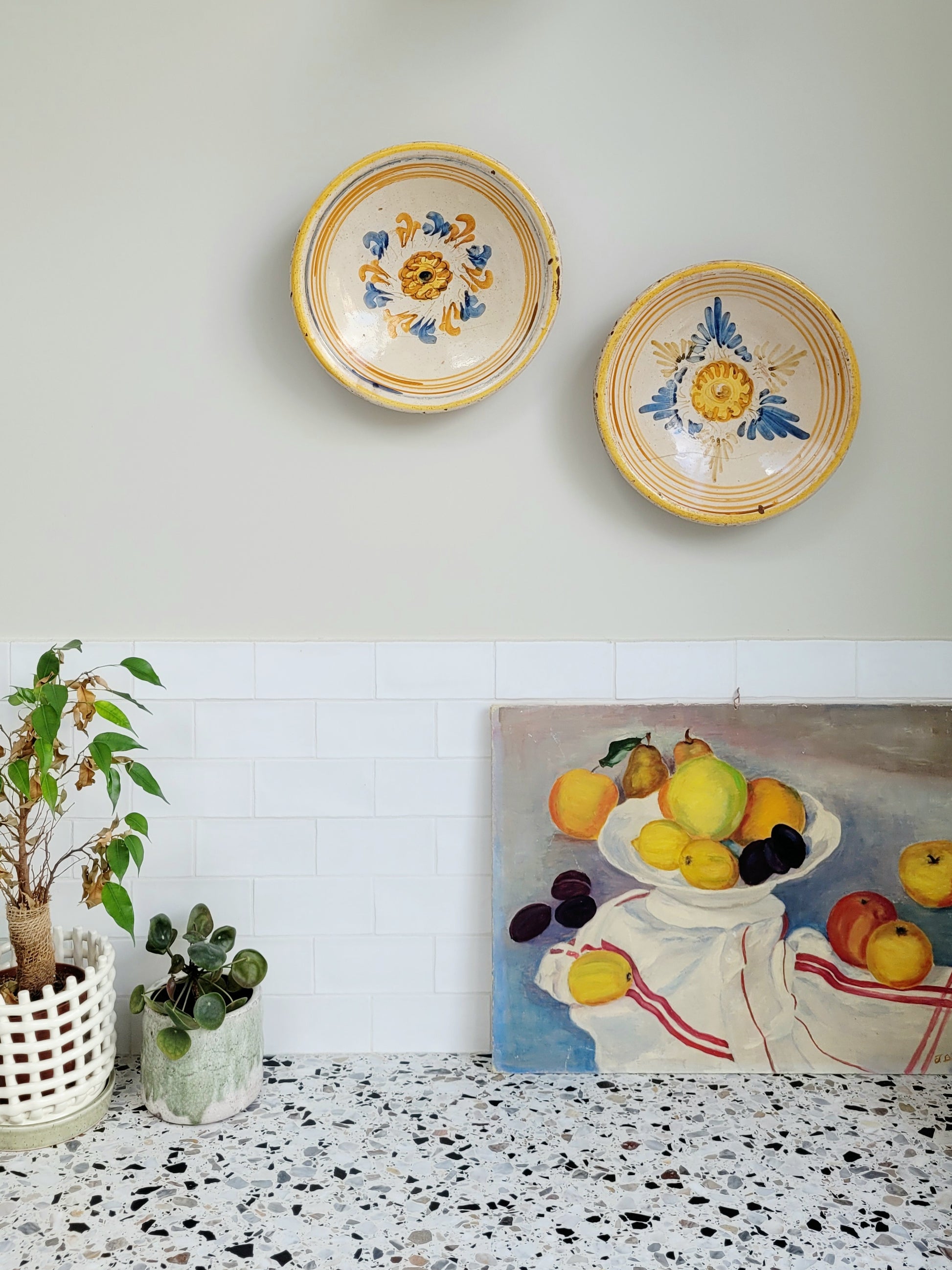 two antique plates hanging on a wall with a vintage painting underneath