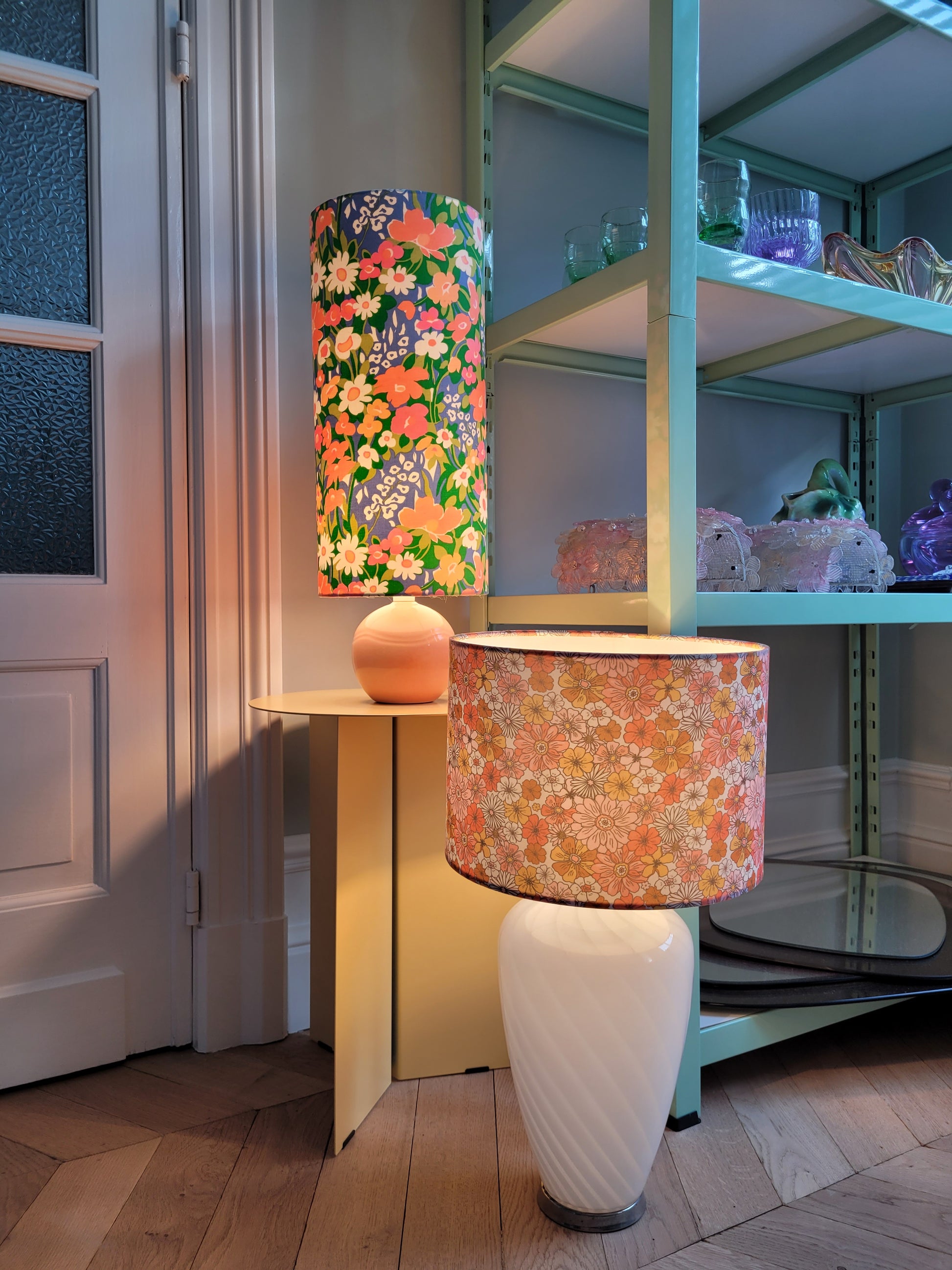 full view of 2 cheerful table lamps with a pink/coral ceramic base paired with an extra-tall, cylindrical fabric lampshade in a lively retro floral print from the 80s.