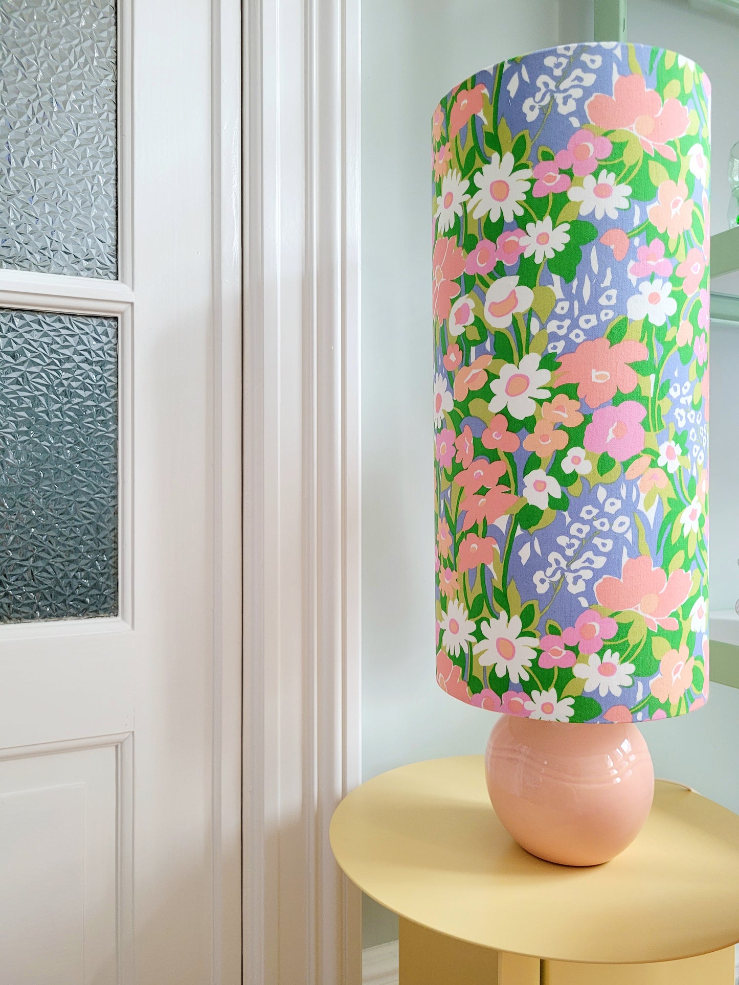 front view of a cheerful table lamp with a pink/coral ceramic base paired with an extra-tall, cylindrical fabric lampshade in a lively retro floral print from the 80s.
