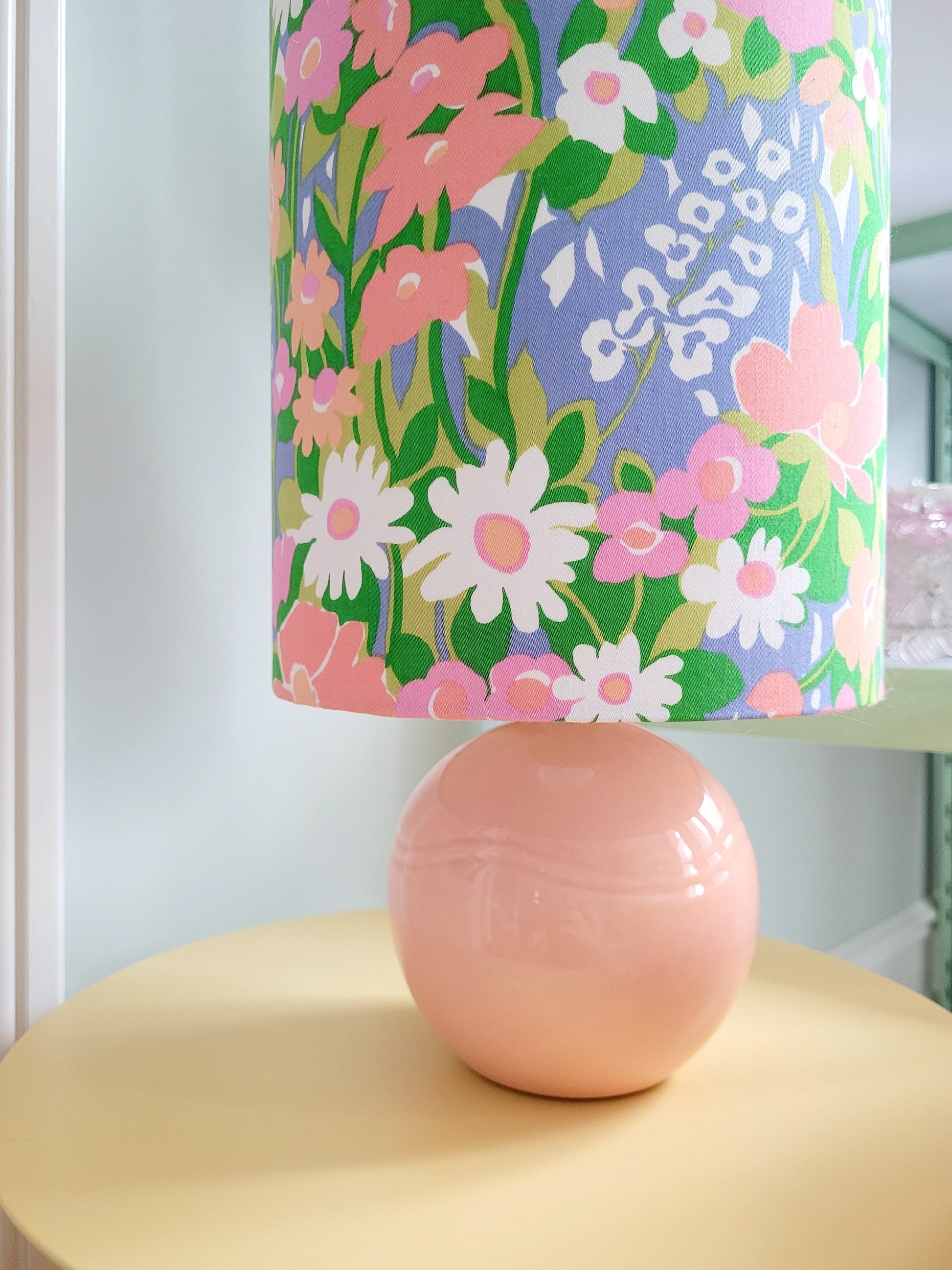 detail of a cheerful table lamp with a pink/coral ceramic base paired with an extra-tall, cylindrical fabric lampshade in a lively retro floral print from the 80s.