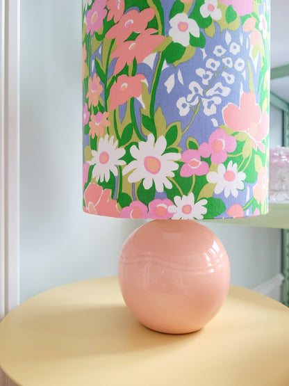 detail of a cheerful table lamp with a pink/coral ceramic base paired with an extra-tall, cylindrical fabric lampshade in a lively retro floral print from the 80s.