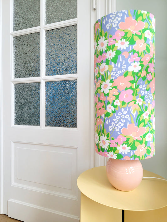 A cheerful table lamp with a pink/coral ceramic base paired with an extra-tall, cylindrical fabric lampshade in a lively retro floral print from the 80s.