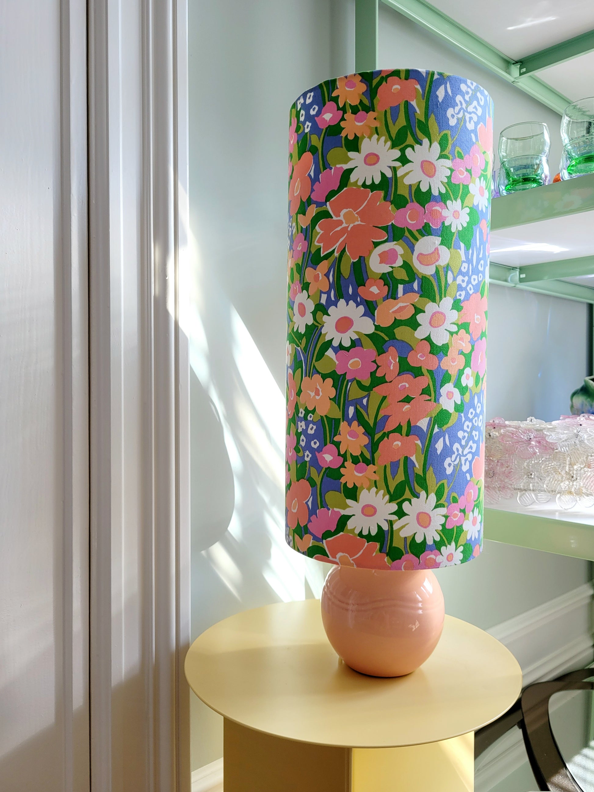 A cheerful table lamp with a pink/coral ceramic base paired with an extra-tall, cylindrical fabric lampshade in a lively retro floral print from the 80s.