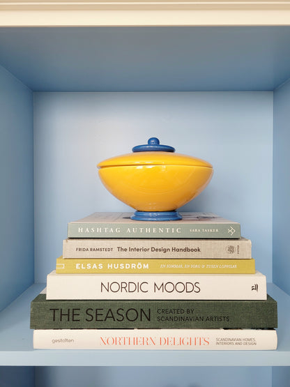 front view of a ceramic jar in blue and yellow on a stack of interior books