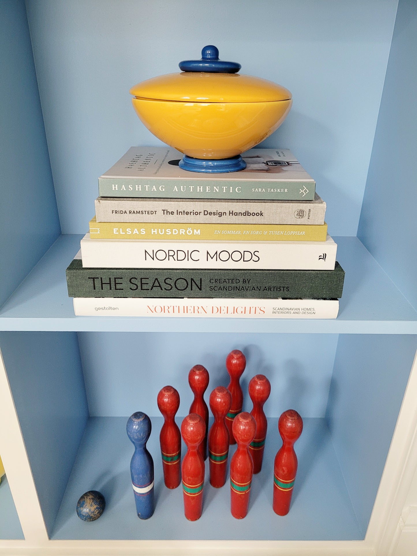 front view of a ceramic jar in blue and yellow on a stack of interior books and a game of skittles