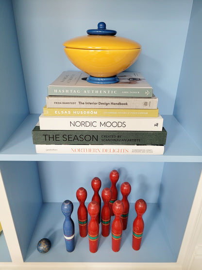 front view of a ceramic jar in blue and yellow on a stack of interior books and a game of skittles