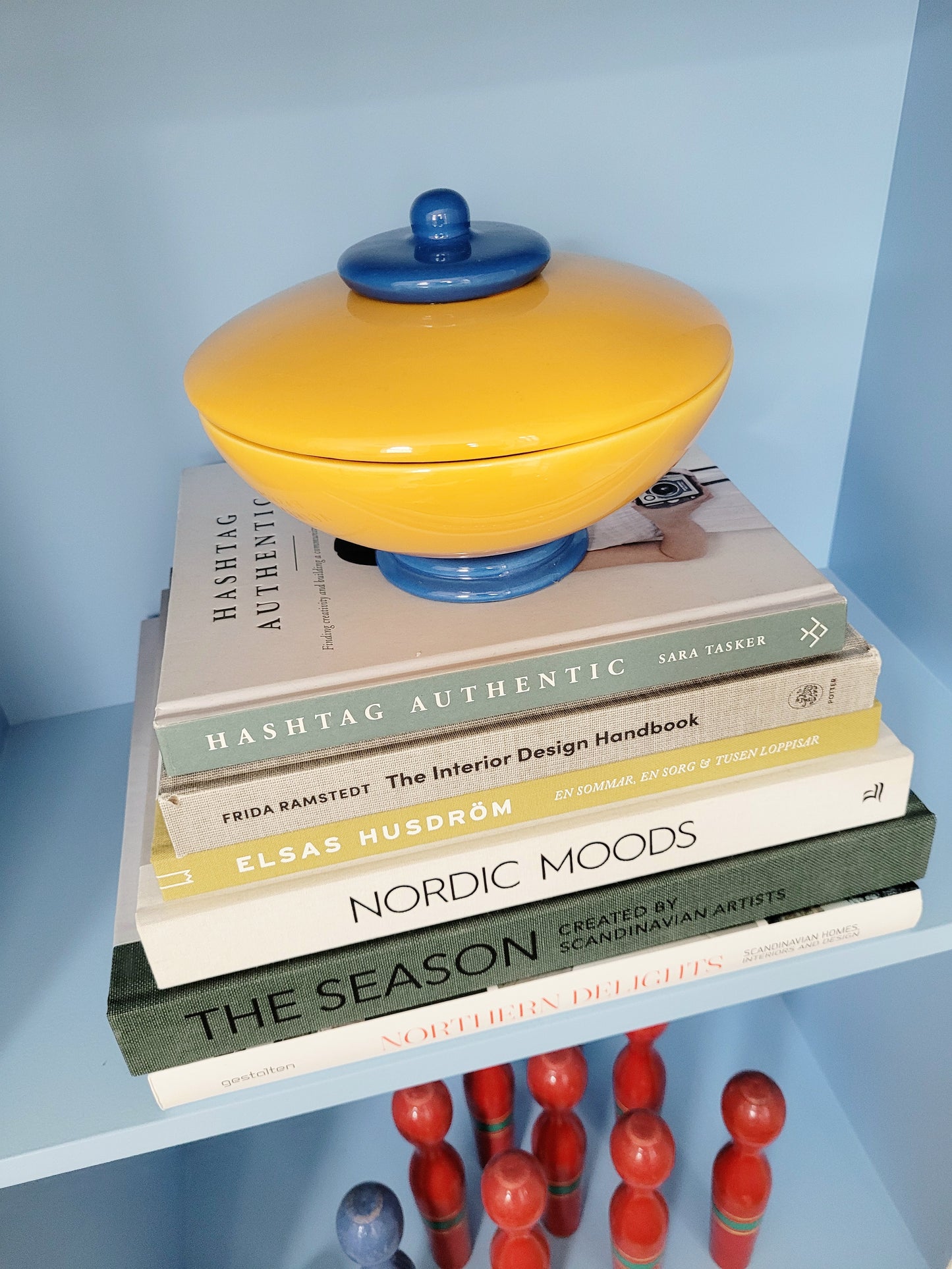 front view of a ceramic jar in blue and yellow on a stack of interior books