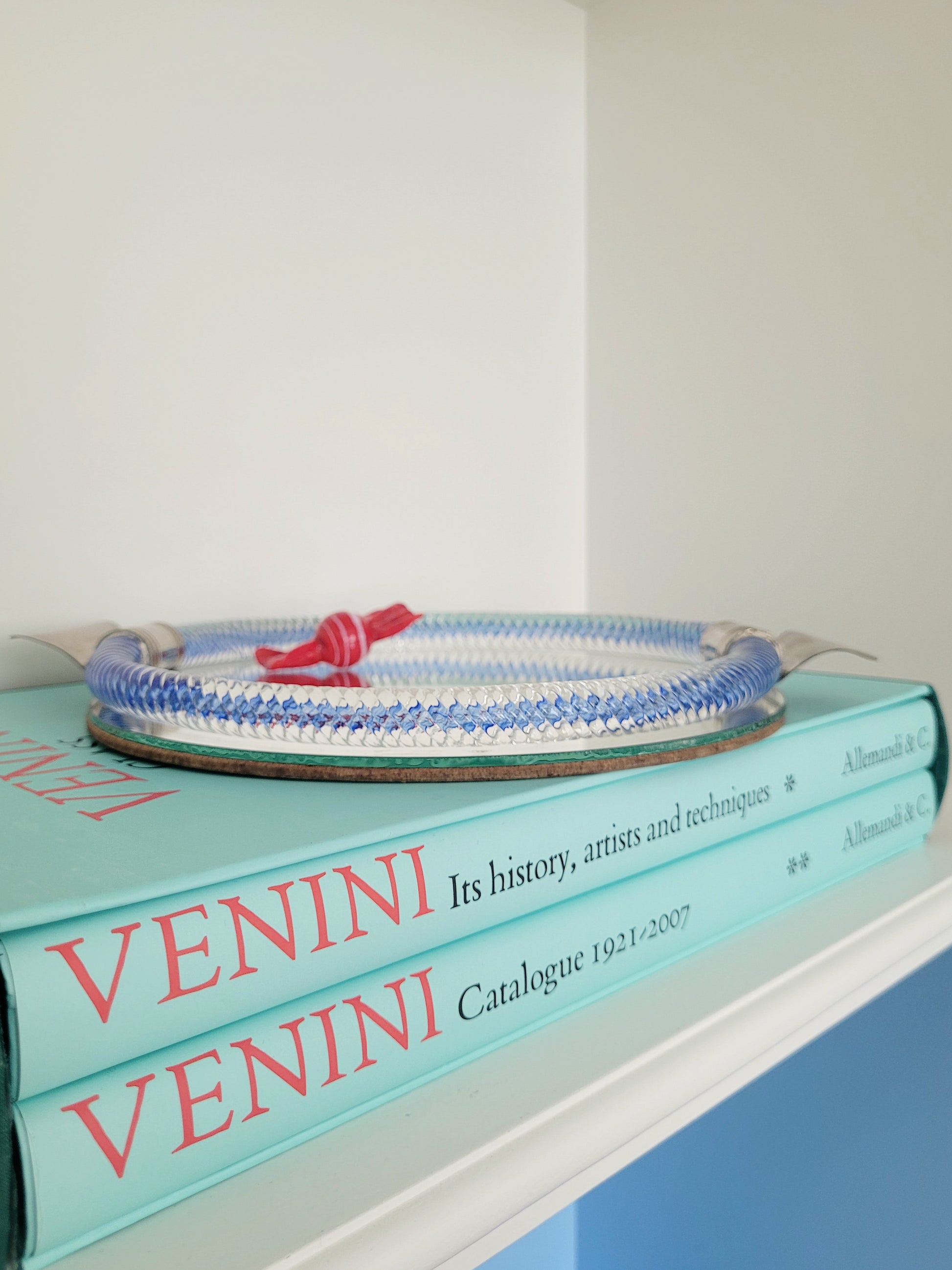 detail of an Italian mirror tray with twisted blue Murano glass frame on a stack of Venini books