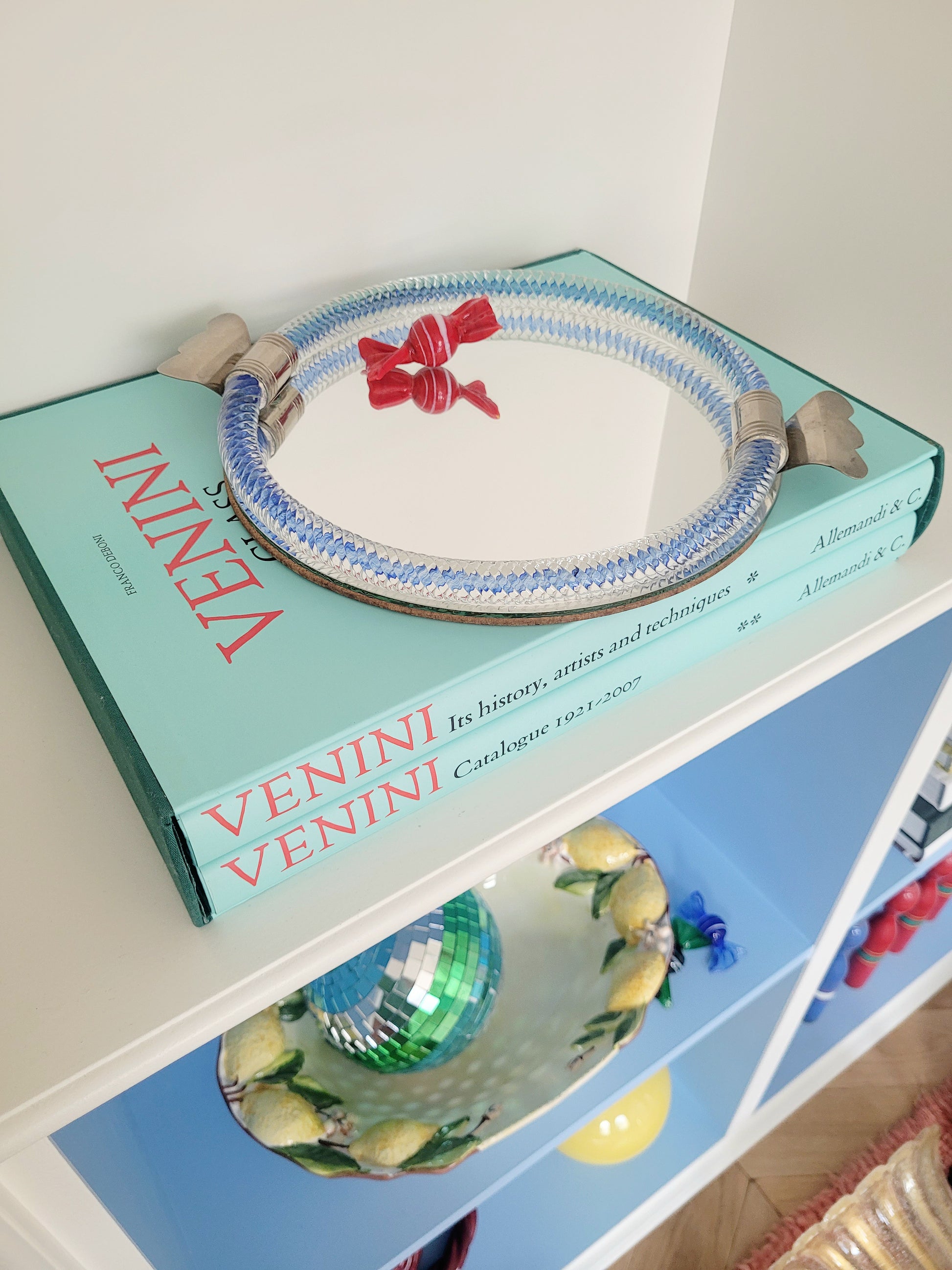 full view of an Italian mirror tray with twisted blue Murano glass frame on a stack of Venini books