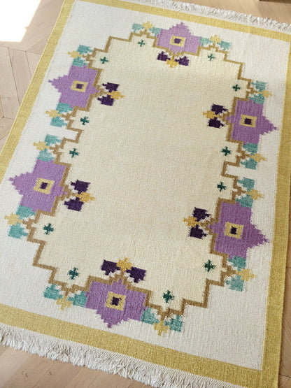 A large flatweave rug in a stunning warm colour palette that incorporates yellow, purple and green