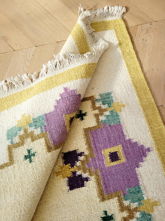 A large flatweave rug in a stunning warm colour palette that incorporates yellow, purple and green