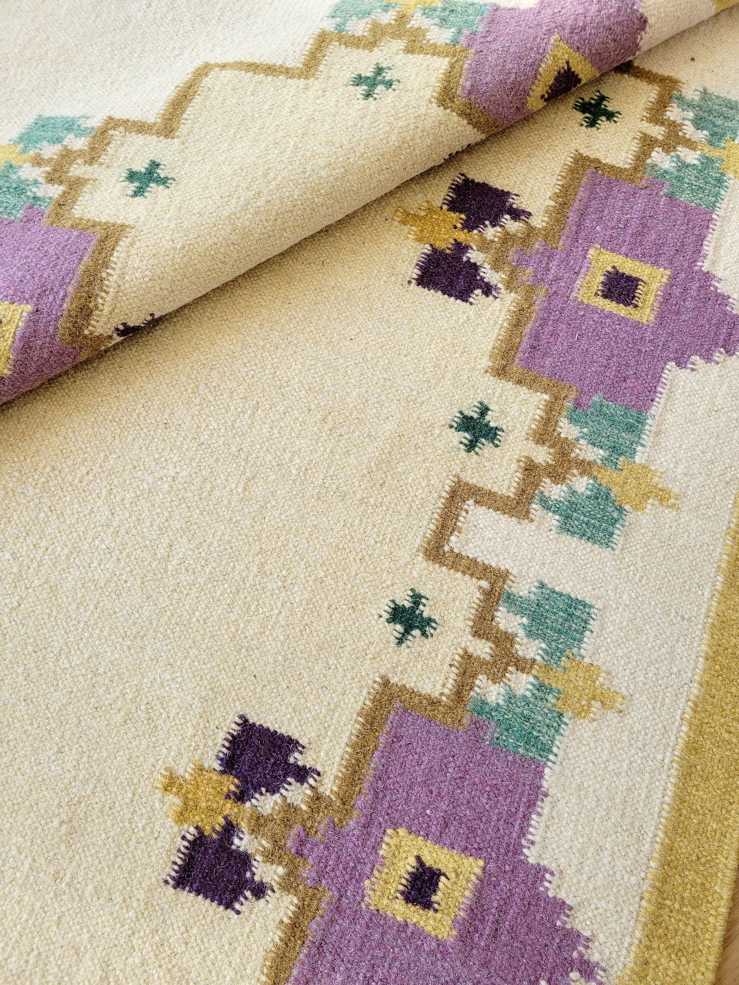 A large flatweave rug in a stunning warm colour palette that incorporates yellow, purple and green
