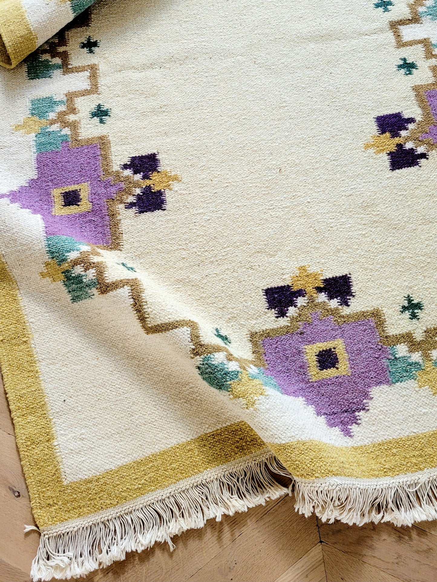 A large flatweave rug in a stunning warm colour palette that incorporates yellow, purple and green