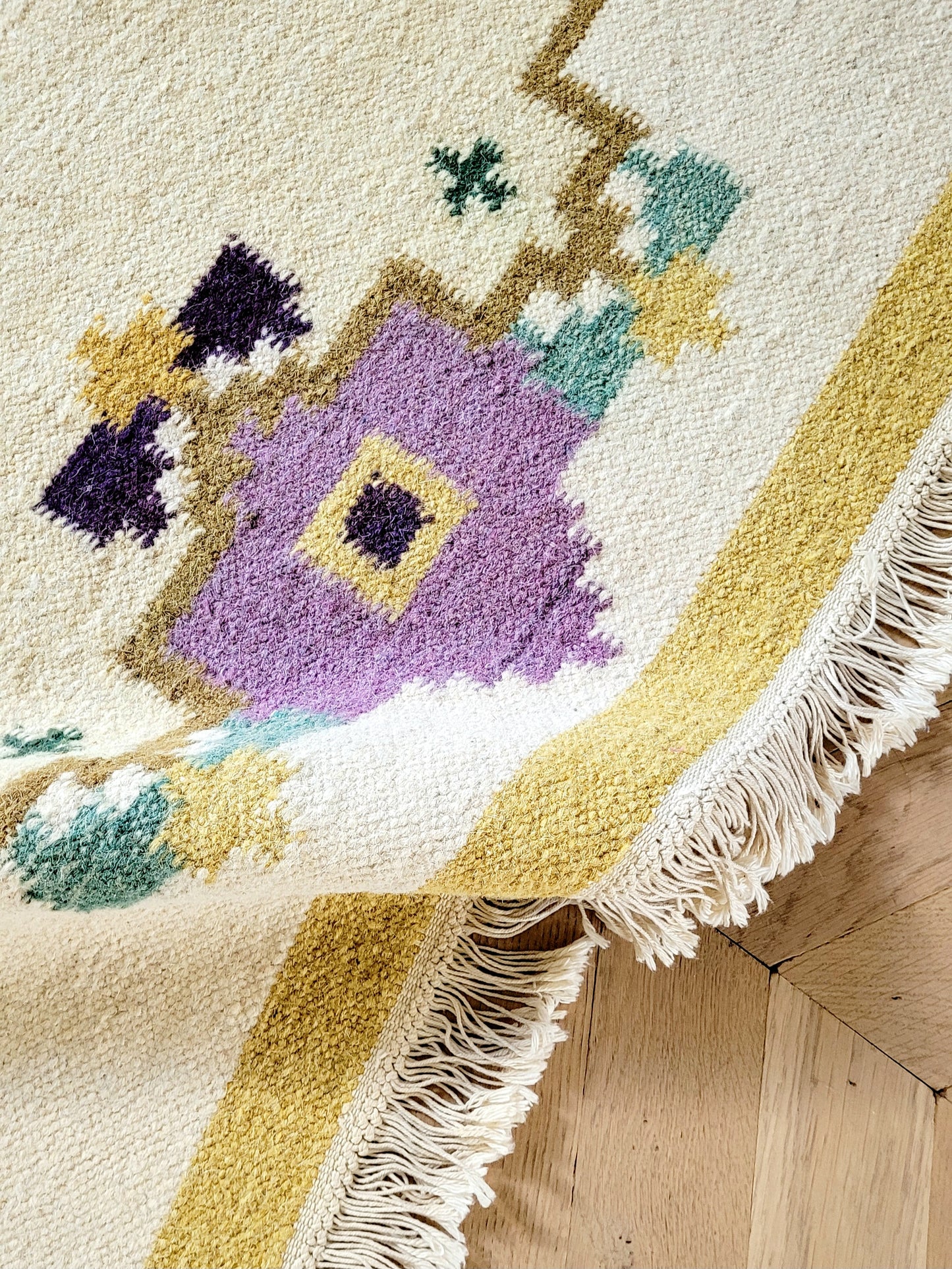 A large flatweave rug in a stunning warm colour palette that incorporates yellow, purple and green