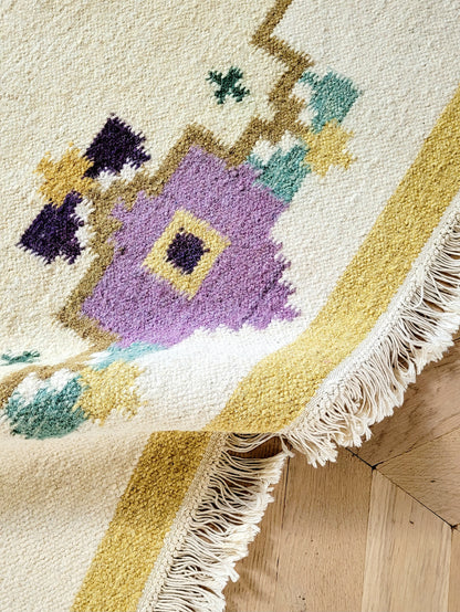 A large flatweave rug in a stunning warm colour palette that incorporates yellow, purple and green