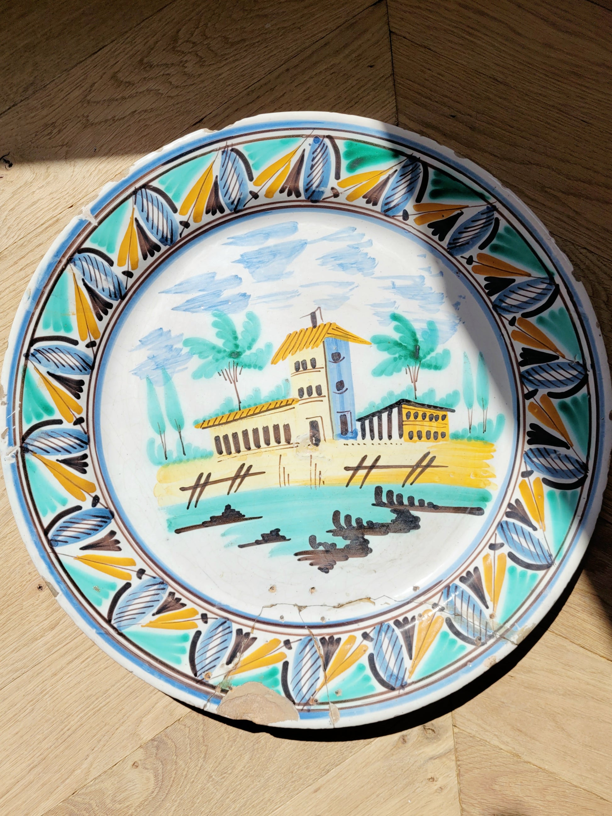 full view of a large hand-painted wall plate with rural landscape on a parquet floor