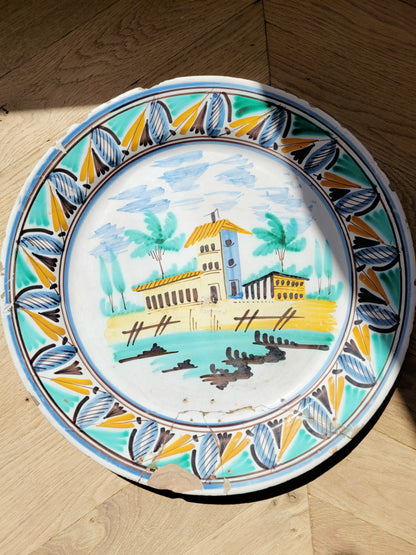 full view of a large hand-painted wall plate with rural landscape on a parquet floor